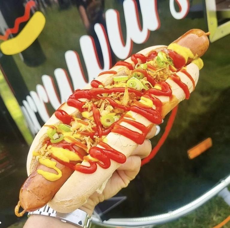 A loaded German hot dog with mustard, ketchup and crispy onions