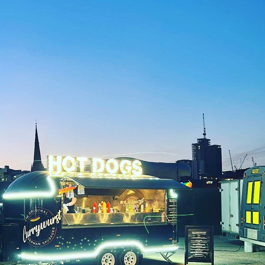 The Currywurst trailer lit up against the Birmingham skyline at dusk